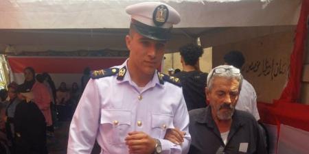 رجل شرطة يساعد مسنا للوصول إلى لجنته الانتخابية فى حدائق القبة - بلس 48